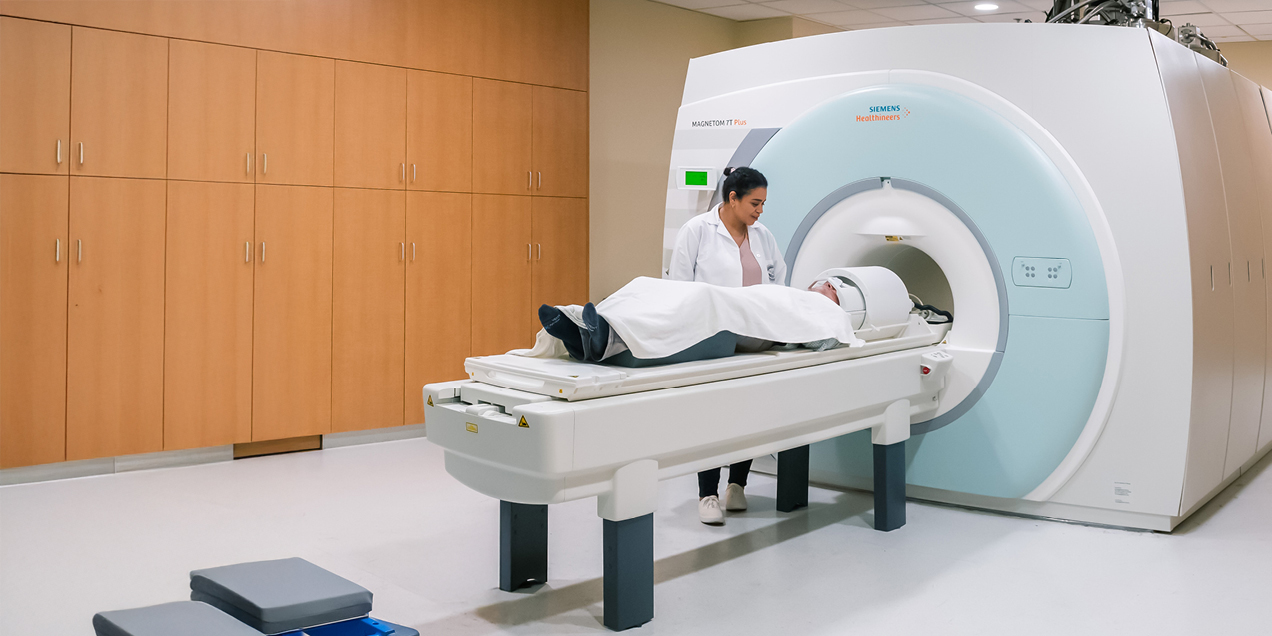 MRI technologist assisting a patient on the table of a Siemens Magnetom 7 Tesla MRI scanner in a modern clinical imaging suite.
