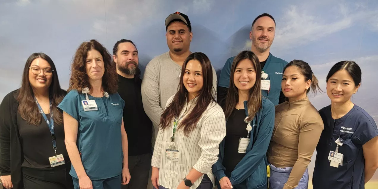 A group of healthcare staff standing together and smiling for a group photo in front of a wall with a sky-themed backdrop.