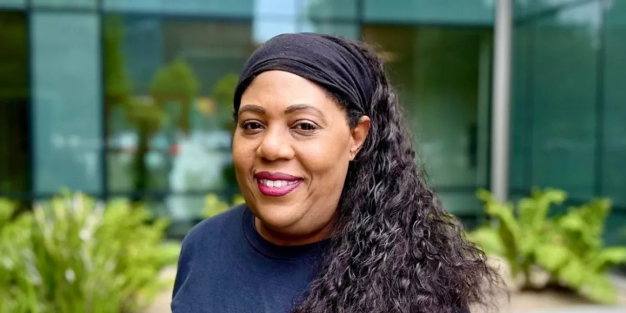 Ingrid Mcgraw smiling with long curly hair wearing a black headband and a navy UCSF Benioff Children’s Hospitals shirt stands outdoors in front of a modern glass building with greenery in the background.