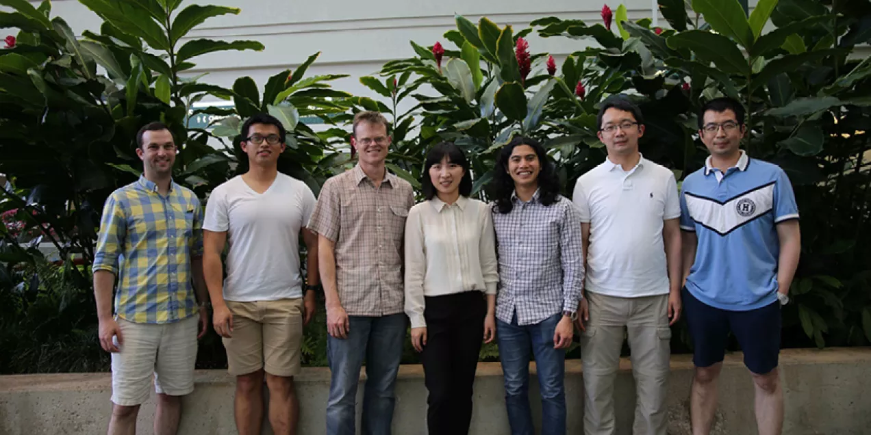Larson Lab group standing outdoors in front of leafy plants.