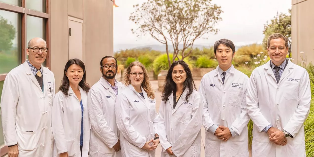 A group of radiology faculty in white coats stand together outdoors on a medical campus, smiling toward the camera.