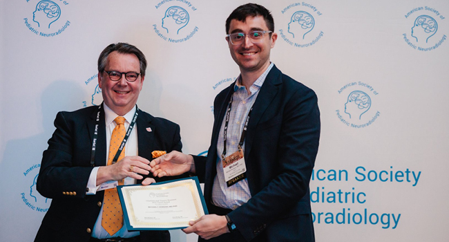Man with glasses recieving an award plaque